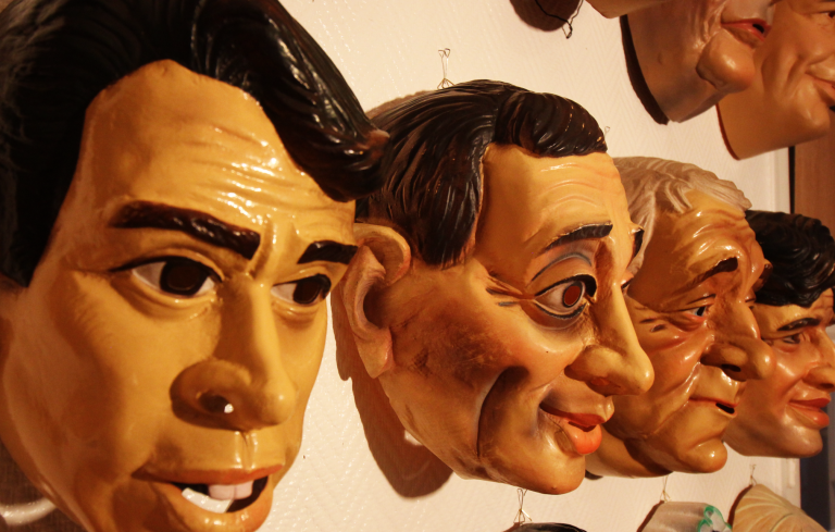 Masques en bois représentant des visages souriants et diversifiés, accrochés au mur.