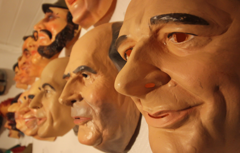 Masques en latex représentant différents visages, alignés sur un mur.