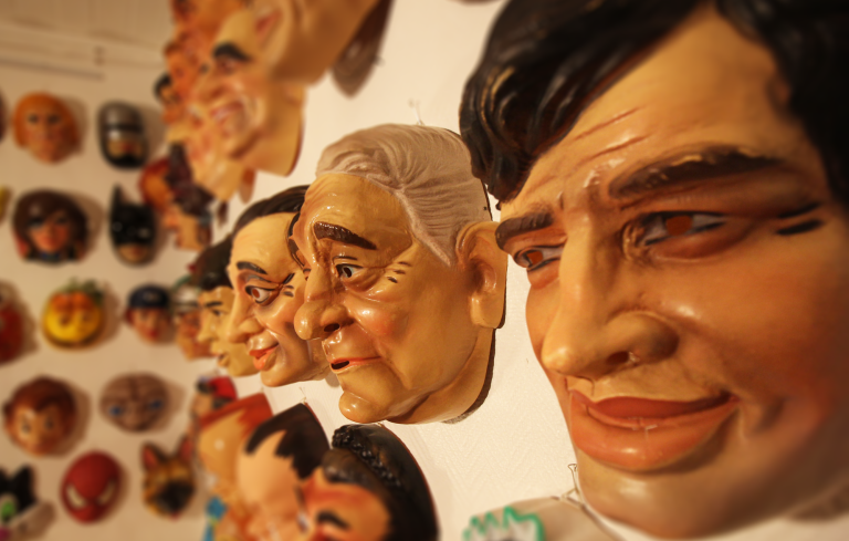Masques en plastique représentant différents visages humains, exposés sur un mur.